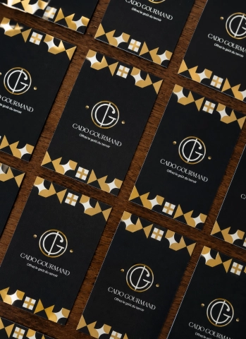 Cartes de visite Cado Gourmand disposées à plat sur un fond bois clair avec finition noire et dorée haut de gamme